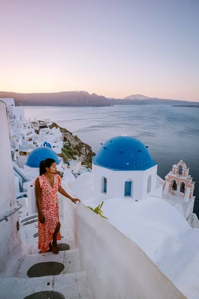 Santorini Görögország, fiatal nő a luxus nyaralás a sziget Santorini nézi napkelte a kék kupola templom és fehérre meszelt falu Oia Santorini Görögország napkeltekor, férfiak és nők a — Stock Fotó