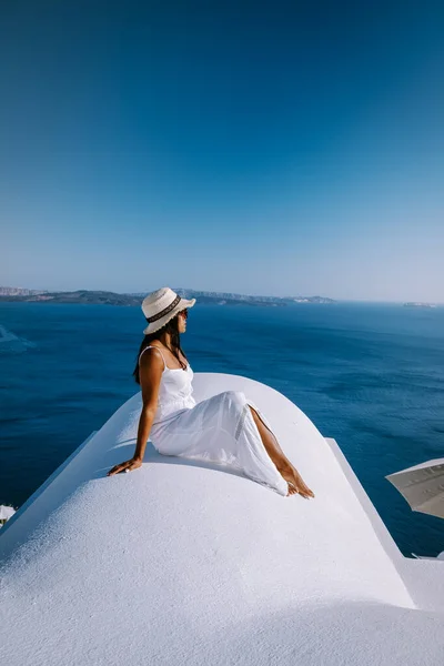 Santorini Greece, young woman on luxury vacation at the Island of Santorini watching sunrise by the blue dome church and whitewashed village of Oia Santorini Greece during sunrise, men and woman on