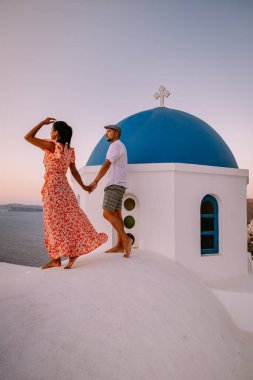 Santorini Yunanistan, genç çift güneş doğarken mavi kubbe kilisesi ve beyazlatılmış Oia Santorini köyünün gündoğumunu izlemek için Santorini Adası 'nda lüks bir tatile çıktılar.