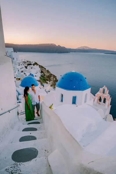 Santorini Greece, young couple on luxury vacation at the Island of Santorini watching sunrise by the blue dome church and whitewashed village of Oia Santorini Greece during sunrise, men and woman on — Stock Photo, Image