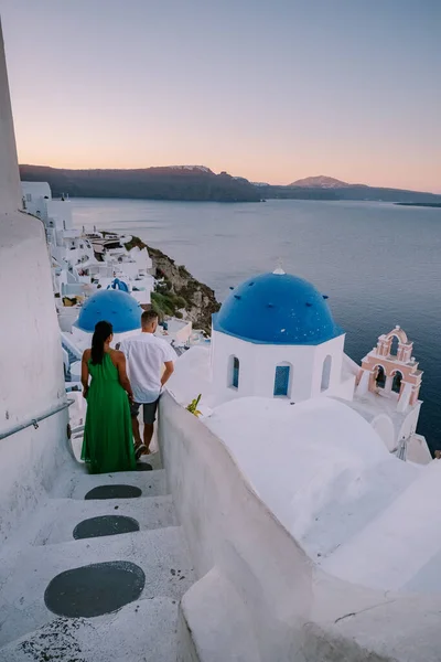 Santorini Grecia, pareja joven en vacaciones de lujo en la isla de Santorini viendo el amanecer por la iglesia de cúpula azul y el pueblo encalado de Oia Santorini Grecia durante el amanecer, hombres y mujeres en — Foto de Stock