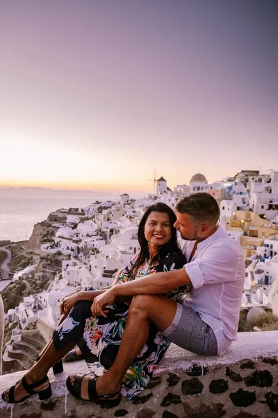 Santorin Grèce, jeune couple en vacances de luxe à l'île de Santorin regardant le lever du soleil près de l'église à dôme bleu et village blanchi à la chaux d'Oia Santorin Grèce pendant le lever du soleil, hommes et femmes sur — Photo