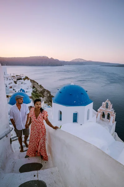 Santorini Görögország, fiatal pár luxus nyaralás a sziget Santorini nézi napkelte a kék kupola templom és fehérre meszelt falu Oia Santorini Görögország napkeltekor, férfiak és nők a — Stock Fotó