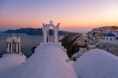Yunanistan 'ın Santorini Adası' nda gün batımı, güzel, bembeyaz bir köy olan Oia 'da gün batımında kilise ve yel değirmeni.