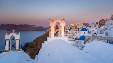 Yunanistan 'ın Santorini Adası' nda gün batımı, güzel, bembeyaz bir köy olan Oia 'da gün batımında kilise ve yel değirmeni.