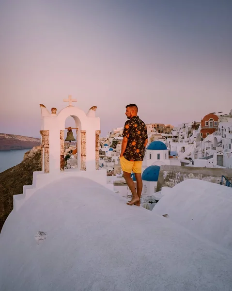 Yunanistan 'ın Santorini Adası' nda gün batımında, güzel, bembeyaz bir köy olan Oia 'da günbatımında kilise ve yel değirmeni, lüks tatilde olan genç erkekler Santorini' de. — Stok fotoğraf