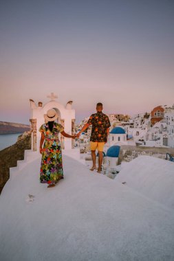 Santorini Yunanistan, genç çift güneş doğarken mavi kubbe kilisesi ve beyazlatılmış Oia Santorini köyünün gündoğumunu izlemek için Santorini Adası 'nda lüks bir tatile çıktılar.