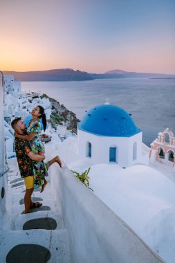 Santorini Yunanistan, genç çift güneş doğarken mavi kubbe kilisesi ve beyazlatılmış Oia Santorini köyünün gündoğumunu izlemek için Santorini Adası 'nda lüks bir tatile çıktılar.