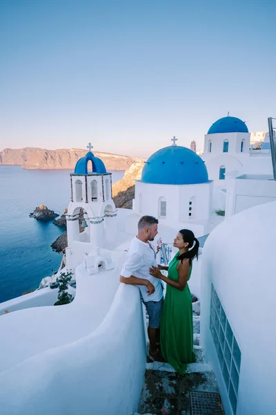 Santorini Grecia, pareja joven en vacaciones de lujo en la isla de Santorini viendo el amanecer por la iglesia de cúpula azul y el pueblo encalado de Oia Santorini Grecia durante el amanecer, hombres y mujeres en — Foto de Stock