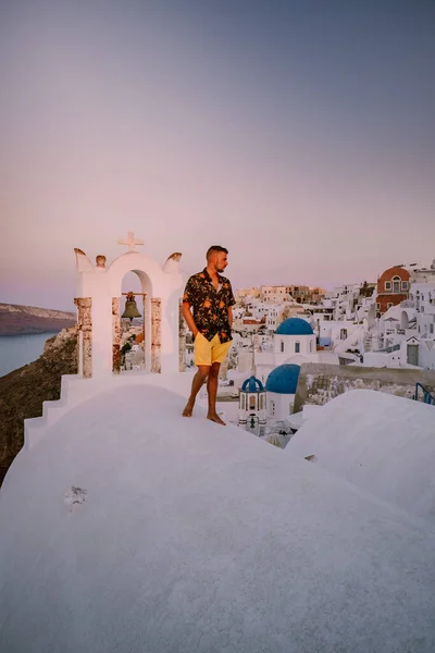 Yunanistan 'ın Santorini Adası' nda gün batımında, güzel, bembeyaz bir köy olan Oia 'da günbatımında kilise ve yel değirmeni, lüks tatilde olan genç erkekler Santorini' de. — Stok fotoğraf