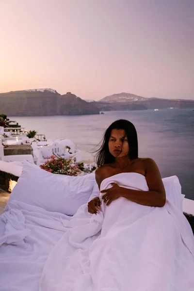 Santorini Greece, young woman on luxury vacation at the Island of Santorini watching sunrise by the blue dome church and whitewashed village of Oia Santorini Greece during sunrise, men and woman on