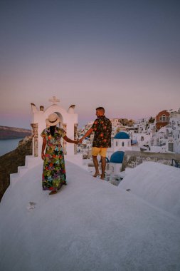 Santorini Yunanistan, genç çift güneş doğarken mavi kubbe kilisesi ve beyazlatılmış Oia Santorini köyünün gündoğumunu izlemek için Santorini Adası 'nda lüks bir tatile çıktılar.