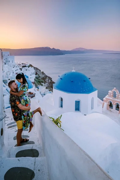 Santorini Greece, young couple on luxury vacation at the Island of Santorini watching sunrise by the blue dome church and whitewashed village of Oia Santorini Greece during sunrise, men and woman on — Stock Photo, Image