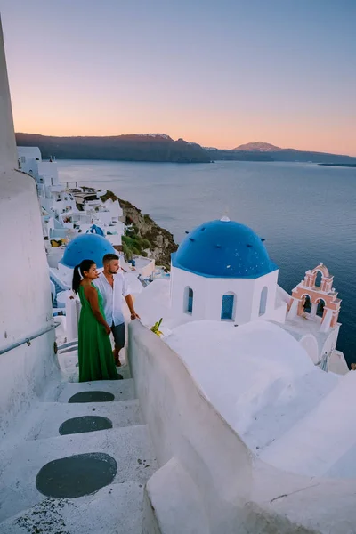 Santorini Grécia, jovem casal em férias de luxo na Ilha de Santorini assistindo ao nascer do sol pela igreja cúpula azul e aldeia caiada de branco de Oia Santorini Grécia durante o nascer do sol, homens e mulheres em — Fotografia de Stock