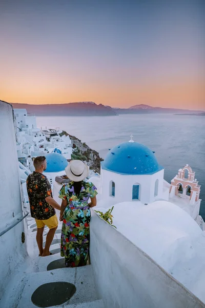 Santorini Grecia, pareja joven en vacaciones de lujo en la isla de Santorini viendo el amanecer por la iglesia de cúpula azul y el pueblo encalado de Oia Santorini Grecia durante el amanecer, hombres y mujeres en — Foto de Stock