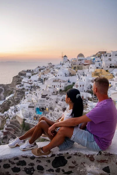 Santorini Greece, young couple on luxury vacation at the Island of Santorini watching sunrise by the blue dome church and whitewashed village of Oia Santorini Greece during sunrise, men and woman on — Stock Photo, Image