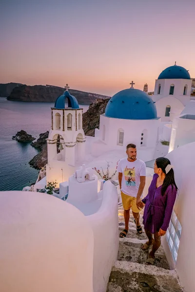 Santorini Görögország, fiatal pár luxus nyaralás a sziget Santorini nézi napkelte a kék kupola templom és fehérre meszelt falu Oia Santorini Görögország napkeltekor — Stock Fotó