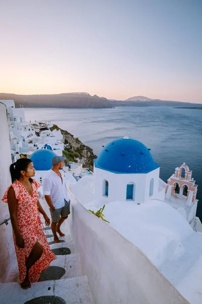 Santorini Grécia, jovem casal em férias de luxo na Ilha de Santorini assistindo ao nascer do sol pela igreja cúpula azul e aldeia caiada de branco de Oia Santorini Grécia durante o nascer do sol, homens e mulheres em — Fotografia de Stock