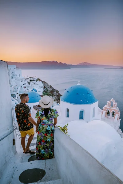 Santorini Görögország, fiatal pár luxus nyaralás a sziget Santorini nézi napkelte a kék kupola templom és fehérre meszelt falu Oia Santorini Görögország napkeltekor, férfiak és nők a — Stock Fotó