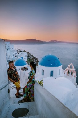 Santorini Yunanistan, genç çift güneş doğarken mavi kubbe kilisesi ve beyazlatılmış Oia Santorini köyünün gündoğumunu izlemek için Santorini Adası 'nda lüks bir tatile çıktılar.