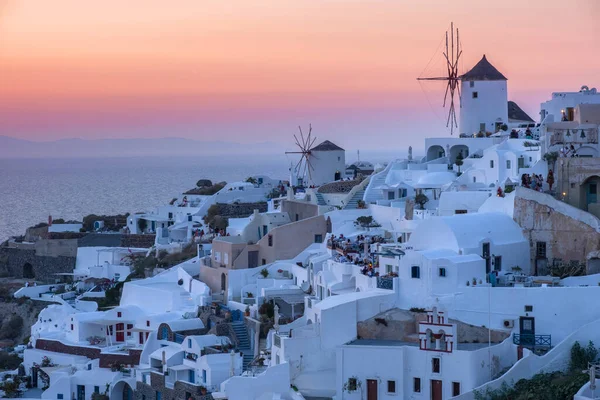 Ηλιοβασίλεμα στο νησί της Σαντορίνης Ελλάδα, όμορφο ασβεστωμένο χωριό Οία με εκκλησία και ανεμόμυλο κατά τη διάρκεια του ηλιοβασιλέματος — Φωτογραφία Αρχείου