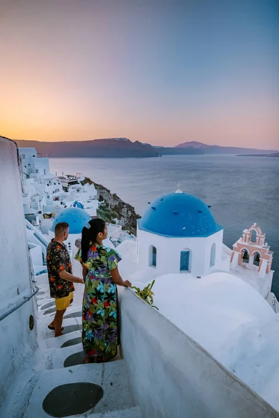 Santorini Greece, young couple on luxury vacation at the Island of Santorini watching sunrise by the blue dome church and whitewashed village of Oia Santorini Greece during sunrise, men and woman on — Stock Photo, Image