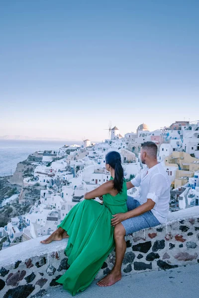 Santorini Greece, young couple on luxury vacation at the Island of Santorini watching sunrise by the blue dome church and whitewashed village of Oia Santorini Greece during sunrise, men and woman on — Stock Photo, Image