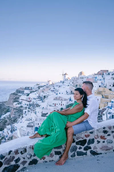 Santorini Greece, young couple on luxury vacation at the Island of Santorini watching sunrise by the blue dome church and whitewashed village of Oia Santorini Greece during sunrise, men and woman on — Stock Photo, Image