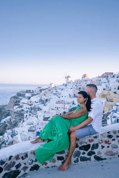 Santorini Grécia, jovem casal em férias de luxo na Ilha de Santorini assistindo ao nascer do sol pela igreja cúpula azul e aldeia caiada de branco de Oia Santorini Grécia durante o nascer do sol, homens e mulheres em — Fotografia de Stock