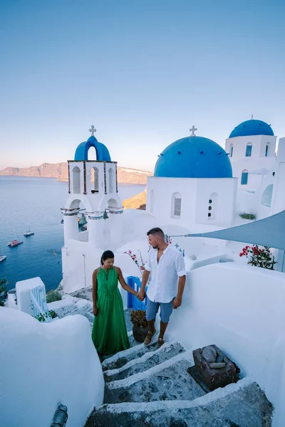 Santorini Grecia, pareja joven en vacaciones de lujo en la isla de Santorini viendo el amanecer por la iglesia de cúpula azul y el pueblo encalado de Oia Santorini Grecia durante el amanecer, hombres y mujeres en — Foto de Stock