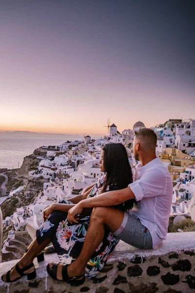 Santorini Grecia, pareja joven en vacaciones de lujo en la isla de Santorini viendo el amanecer por la iglesia de cúpula azul y el pueblo encalado de Oia Santorini Grecia durante el amanecer, hombres y mujeres en —  Fotos de Stock