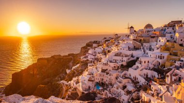 Yunanistan 'ın Santorini Adası' nda gün batımı, güzel, bembeyaz bir köy olan Oia 'da gün batımında kilise ve yel değirmeni.