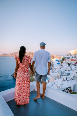 Santorini Yunanistan, genç çift güneş doğarken mavi kubbe kilisesi ve beyazlatılmış Oia Santorini köyünün gündoğumunu izlemek için Santorini Adası 'nda lüks bir tatile çıktılar.
