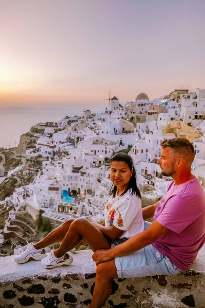 Santorini Greece, young couple on luxury vacation at the Island of Santorini watching sunrise by the blue dome church and whitewashed village of Oia Santorini Greece during sunrise, men and woman on — Stock Photo, Image