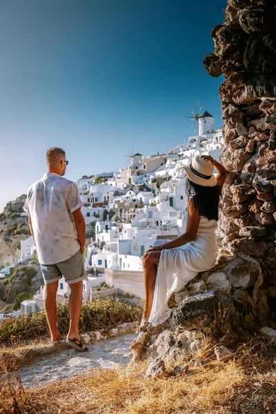 Santorini Grecia, pareja joven en vacaciones de lujo en la isla de Santorini viendo el amanecer por la iglesia de cúpula azul y el pueblo encalado de Oia Santorini Grecia durante el amanecer, hombres y mujeres en — Foto de Stock