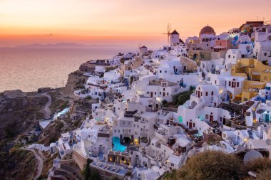 Yunanistan 'ın Santorini Adası' nda gün batımı, güzel, bembeyaz bir köy olan Oia 'da gün batımında kilise ve yel değirmeni.