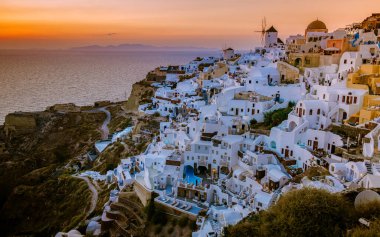 Yunanistan 'ın Santorini Adası' nda gün batımı, güzel, bembeyaz bir köy olan Oia 'da gün batımında kilise ve yel değirmeni.
