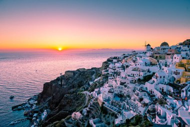 Yunanistan 'ın Santorini Adası' nda gün batımı, güzel, bembeyaz bir köy olan Oia 'da gün batımında kilise ve yel değirmeni.