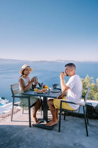 Couple having breakfast at traditional cave house Santorini Greece, beautiful whitewashed village Oia with church and windmill during sunset — Stock Photo, Image