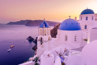 Yunanistan 'ın Santorini Adası' nda gün batımı, güzel, bembeyaz bir köy olan Oia 'da gün batımında kilise ve yel değirmeni.