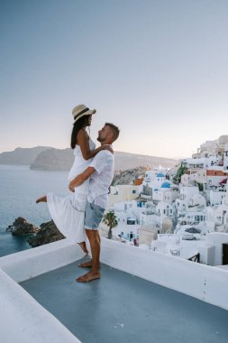 Santorini Yunanistan, Santorini Adası 'nda lüks tatilde olan genç bir çift mavi kubbe kilisesi ve beyazlatılmış Oia Santorini Yunanistan köyünün doğuşunu izliyor. 