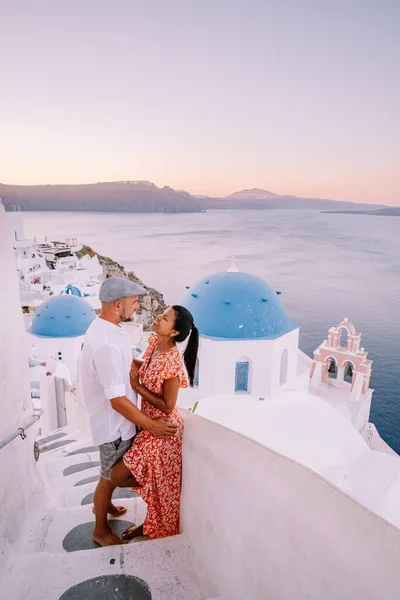 Santorini Greece, young couple on luxury vacation at the Island of Santorini watching sunrise by the blue dome church and whitewashed village of Oia Santorini Greece — Stock Photo, Image