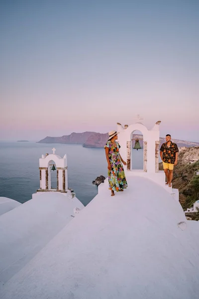 圣托里尼希腊，一对年轻夫妇在圣托里尼岛上观看着蓝色穹顶教堂的日出，和粉刷过的希腊奥亚圣托里尼村 — 图库照片