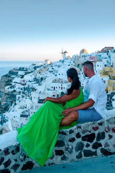 圣托里尼希腊，一对年轻夫妇在圣托里尼岛上观看着蓝色穹顶教堂的日出，和粉刷过的希腊奥亚圣托里尼村 — 图库照片