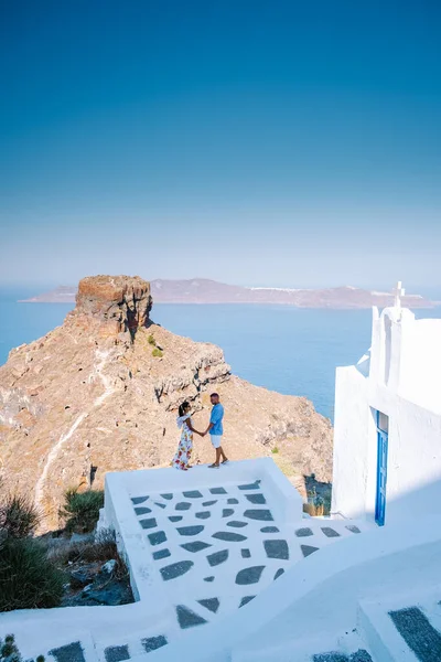 Couple visit Skaros rock Fira, Santorini Greece, young couple on luxury vacation at the Island of Santorini watching sunrise by the blue dome church and whitewashed village of Oia Santorini Greece — Stock Photo, Image