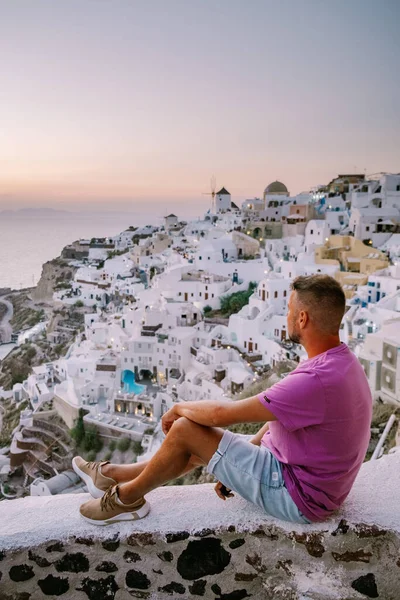 Young men watching sunset Santorini Greece, young couple on luxury vacation at the Island of Santorini watching sunrise by the blue dome church and whitewashed village of Oia Santorini Greece — Stock Photo, Image