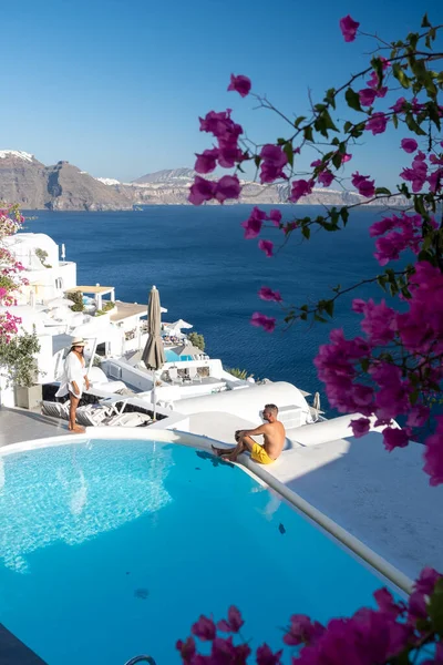 Para na luksusowym basenie infinity, Antorini Grecja, młoda para na luksusowych wakacjach na wyspie Santorini oglądająca wschód słońca przy błękitnym kościele kopuły i bielonej wiosce Oia Santorini Grecja — Zdjęcie stockowe