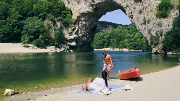 Couple sur la plage au bord de la rivière dans l'Ardèche France Pont d'Arc, Ardèche France, vue de l'arche Narural à Vallon Pont Darc dans le canyon de l'Ardèche en France Europe — Video