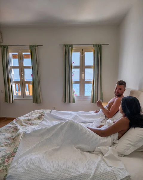 Koppel in wit bed met uitzicht op de oceaan tijdens luxe vakantie in Griekenland — Stockfoto