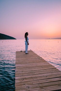 Girit Yunanistan 'da, birbirine aşık genç romantik çift gün doğumunda altın gökyüzü eşliğinde kumsaldaki ahşap iskelede oturup sarılıyor. Tatil ve seyahat konsepti. Deniz kenarında flört eden romantik genç çift